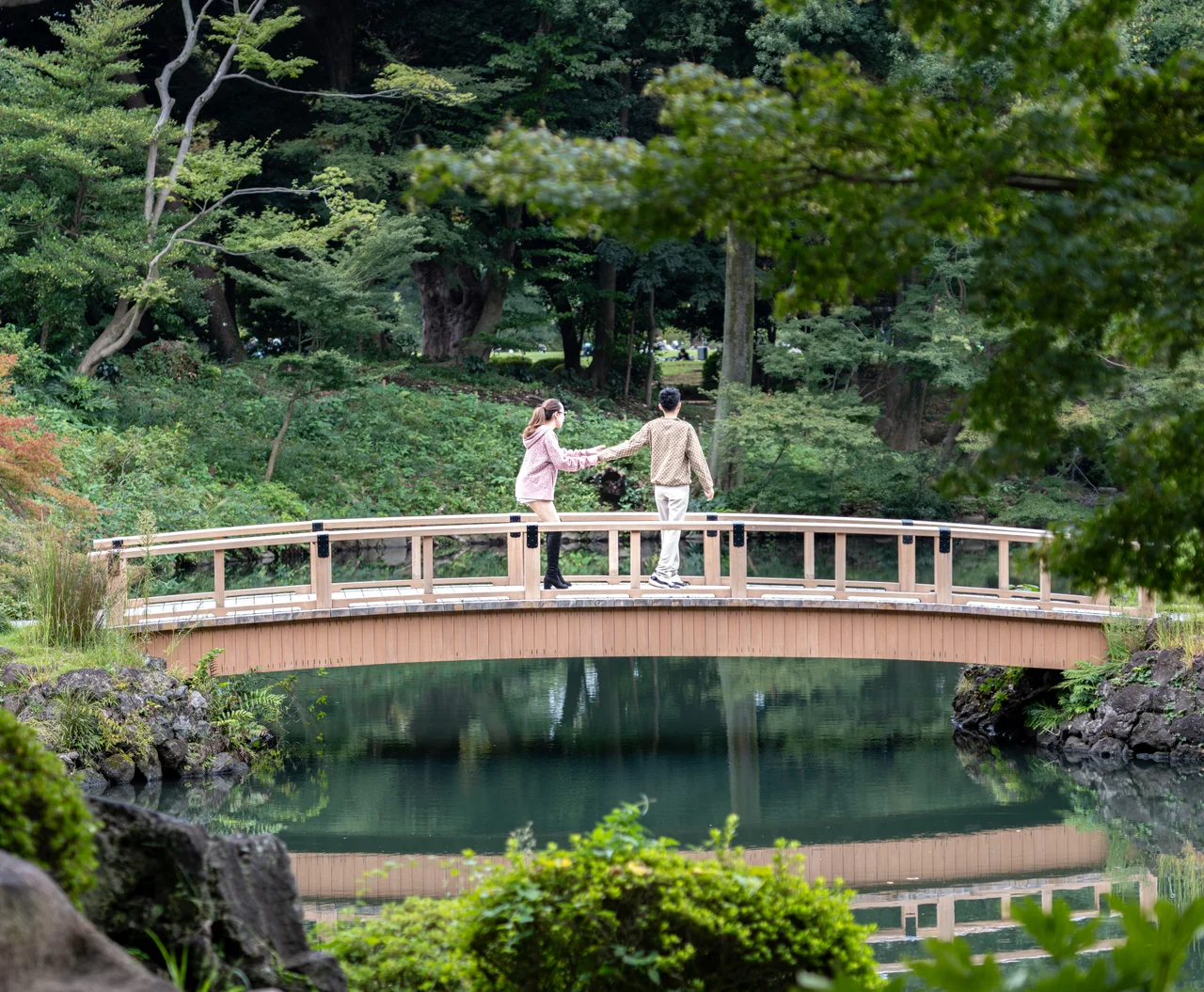 Un couple se tient la main sur un pont de bois au-dessus d'un étang, dans un jardin japonais.