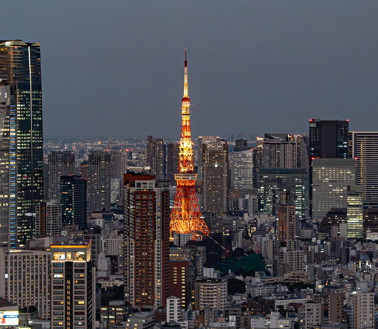 La tour de Tokyo illuminée en orange au milieu des immeubles, à la tombée de la nuit.