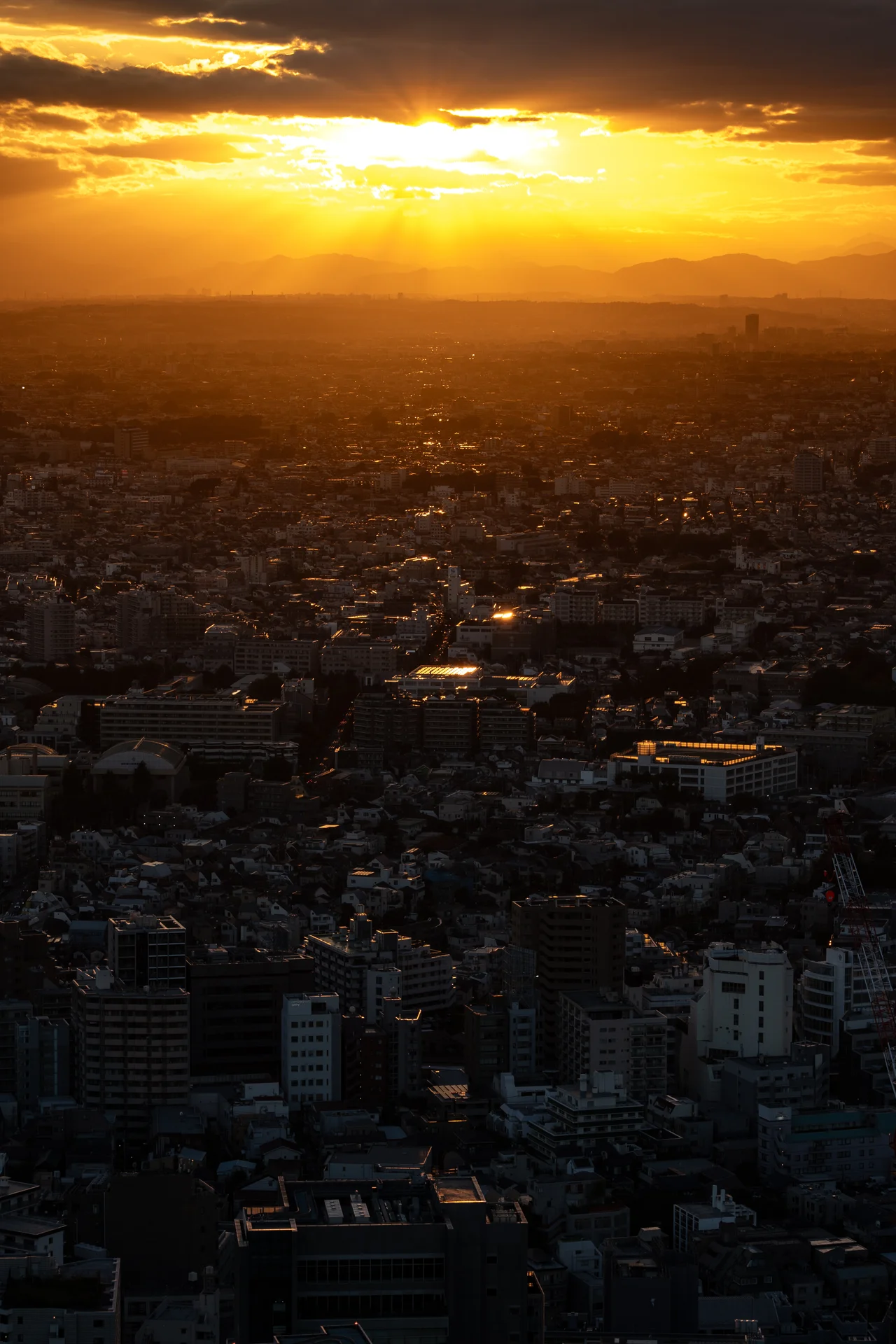 Le soleil couchant perce les nuages au-dessus de Tokyo, qui s'étend dans l'ombre jusqu'à l'horizon.